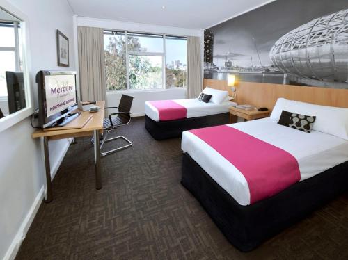 a hotel room with two beds and a desk at Mercure North Melbourne in Melbourne