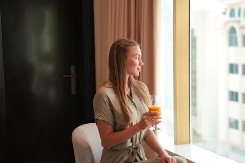 a woman holding a glass of orange juice looking out the window at AG Hotel in Abu Dhabi