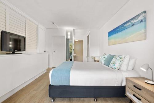 a white bedroom with a bed and a tv at Charlesworth Bay Beach Resort in Coffs Harbour