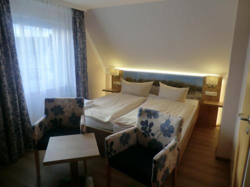 a hotel room with a bed and two chairs at Hotel Pension Am Hafen in Norddeich