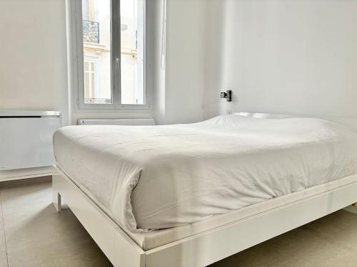 un lit blanc dans une chambre blanche avec une fenêtre dans l'établissement Cannes Appartement 1 chambre - 26H, à Cannes