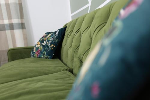 a green couch with a blue pillow on it at 3BR Luxury Stay Near Billing Aquadrome - Elegant 3-Bedrooms One-and-Half Bathrooms Home - Sleeps 8 - Free Parking and Complimentary Access to Billing Aquadrome Holiday Village in Northampton