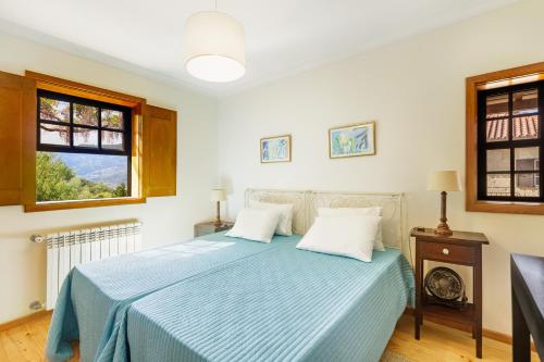 a bedroom with a bed with a blue comforter and two windows at Villa no Douro - Quinta de Pias in Cinfães