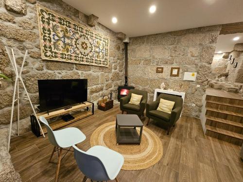a living room with a stone wall with chairs and a television at Quinta da Casa dos Santos - Inside Gerês in Geres