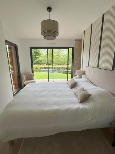 Cette chambre comprend un grand lit blanc et une grande fenêtre. dans l'établissement Un havre de paix au pied du Golf, à Saint-Martin-du-Vieux-Bellême