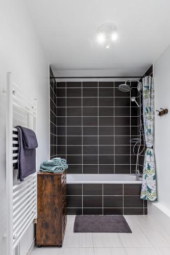 La salle de bains est pourvue d'une baignoire carrelée de noir et d'une douche. dans l'établissement Chez Julia et Kevin, à Serris