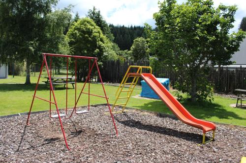 a playground with two swings and a slide at Fairy Springs Motel in Rotorua