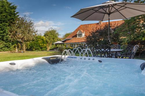 a hot tub with an umbrella in a yard at Catton Old Hall Norwich in Norwich