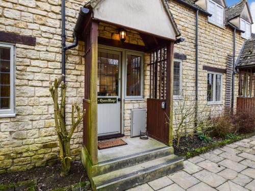 a brick house with a wooden door and stairs at Queen Mary in Winchcombe