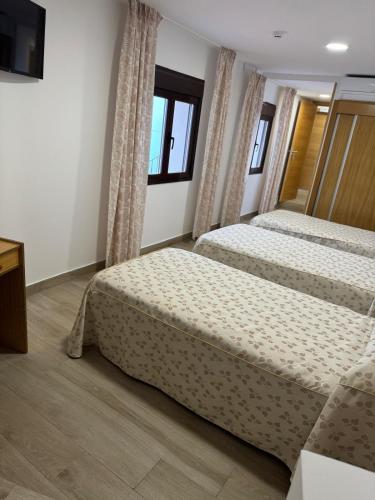 two beds in a room with two windows at Hostal de Cazalegas in Cazalegas