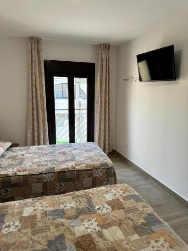 a bedroom with two beds and a tv and a window at Hostal de Cazalegas in Cazalegas