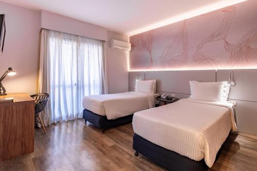 a hotel room with two beds and a window at Intercity Interative São Paulo Jardins in São Paulo