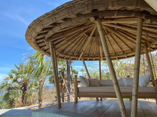a couch under a straw umbrella on a deck at Villas Bukit Lipah in Amed