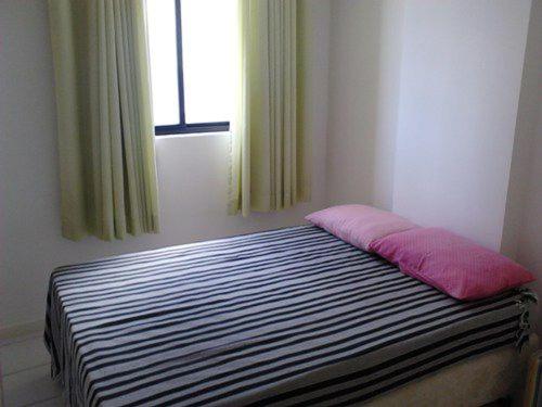 a bed with a pink pillow in a room with a window at Pajucara Flat in Maceió