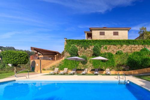 a pool with chairs and umbrellas in front of a house at Villa no Douro - Quinta de Pias in Cinfães