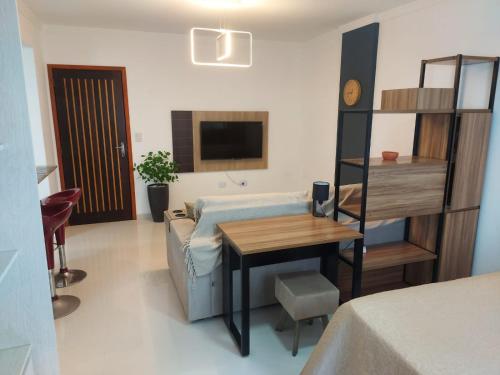 um quarto com um sofá, uma mesa e uma televisão em Apartamento Estúdio em Caraguatatuba com Garagem em Caraguatatuba