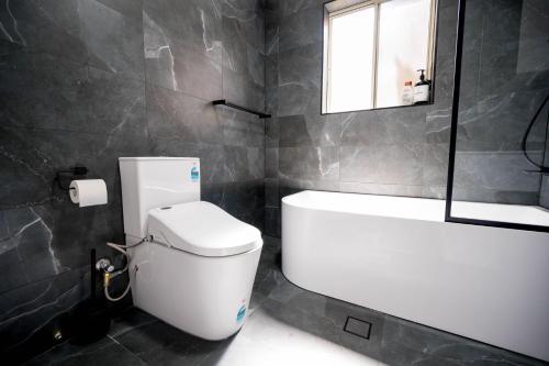 a bathroom with a toilet and a tub and a window at The Driscoll - Modern Smart Villa in West Tamworth