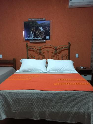 a bed with an orange blanket and white pillows at Pousada Cachoeiras do Cipó in Serra do Cipo