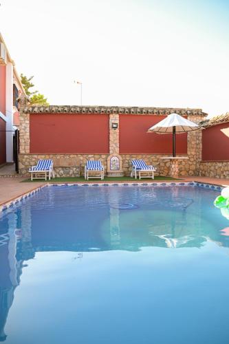 a swimming pool with two chairs and an umbrella at Casa Rural LA ENCINA in Hornachuelos