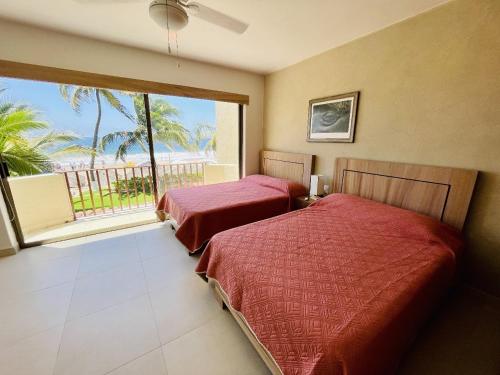 two beds in a room with a large window at Villa 8 frente al mar in Zihuatanejo