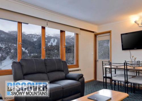 a living room with a couch and a tv and windows at Karoonda 5 - Thredbo in Thredbo