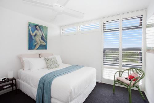 Un dormitorio blanco con una cama y una silla. en Treetop Retreat Five Minute Stroll To The Beach, en Sídney