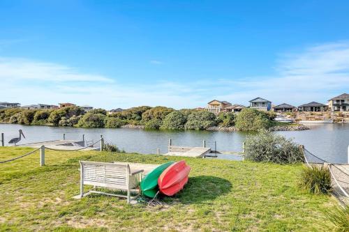 a bench and a boat on the grass next to a river at Lazy Lodge on Blanche - A Family Escape on the River in Hindmarsh Island