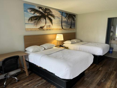 a hotel room with two beds and a desk and a picture of a beach at Rodeway Inn in Owensboro