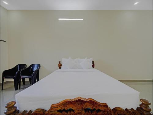 a bedroom with a large white bed with two chairs at Super Hotel O Vsv Guest House in Chennai