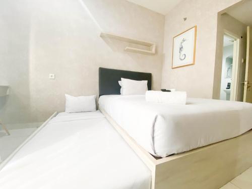 Dos camas en un dormitorio con sábanas blancas. en Elegant and Homey Studio at Amartha View Apartment By Travelio, en Semarang