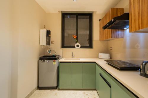 a small kitchen with green cabinets and a refrigerator at ELIVAAS 1 BHK with Rooftop Pool - Kamerios Verano in Goa
