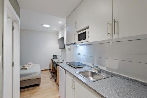 a kitchen with white cabinets and a sink and a bed at Lovely studio fully equipped near subway N9 in Lisbon