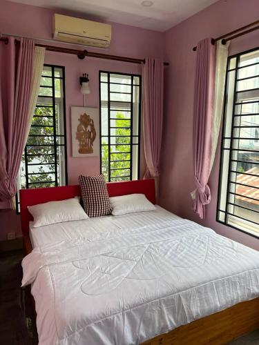 a bedroom with a large bed with pink walls and windows at Kalinga Art Home Guest House in Siem Reap
