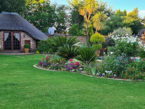a garden with flowers and a stone house at Feathers Guest House in Middelburg