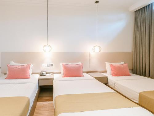 a hotel room with three beds with pink pillows at A Hotel Joo Chiat in Singapore