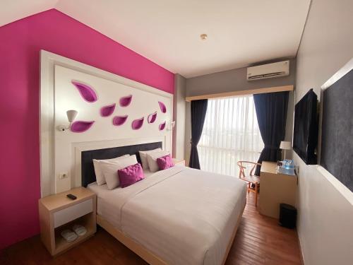 a bedroom with a large bed with pink walls at Shakti Hotel Bandung in Bandung