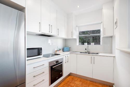 a white kitchen with white cabinets and a microwave at Bondi Getaway - Parking and Walk to the Beach in Sydney