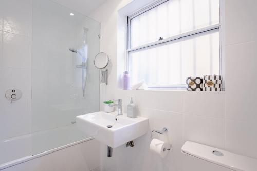 a white bathroom with a sink and a window at Bondi Getaway - Parking and Walk to the Beach in Sydney