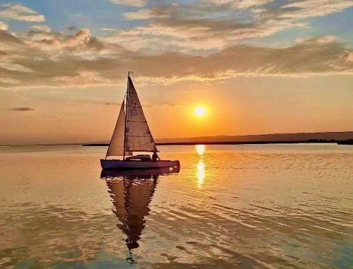 a small sail boat in the water at sunset at Apartments C'EST LA SEA - Whirlpool-Suite oder Dachterrassen-Suite in Neusiedl am See