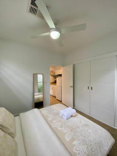 a white bedroom with a bed and a ceiling fan at East Woonona Sea Esta Studio in Woonona