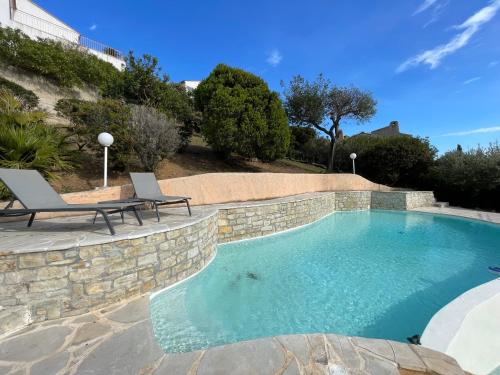 une piscine avec deux chaises et un mur en pierre dans l'établissement Villa Aquarelle, à La Garonnette-Plage