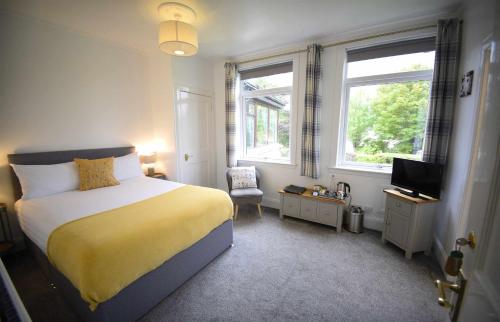 a bedroom with a bed and a tv and two windows at Atholl House Skye in Dunvegan