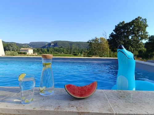 - une table avec deux bouteilles et une pastèque à côté de la piscine dans l'établissement Villa pont d'arc, à Vallon-Pont-dʼArc