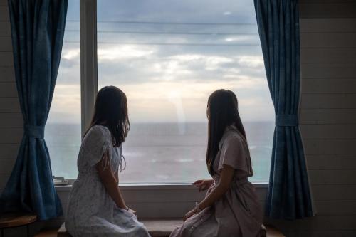 two girls sitting in a window looking out at the ocean at HOMIE TERRACE Funakata in Tateyama
