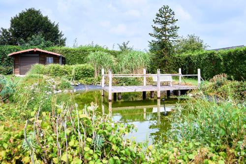 un banc en bois assis sur un pont au-dessus d'un étang dans l'établissement VILLA ARCADIA - Piscine - Spa - Sauna - Cinéma - Jeux d'arcades - Jeux vidéo - Bassin naturel - Jardin, à Seclin