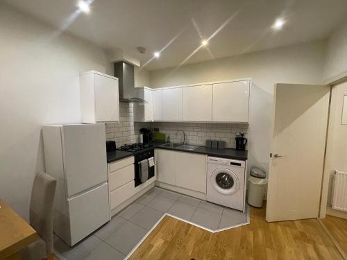 a kitchen with white cabinets and a washer and dryer at Modern apartment 4 mins from Gatwick in Horley