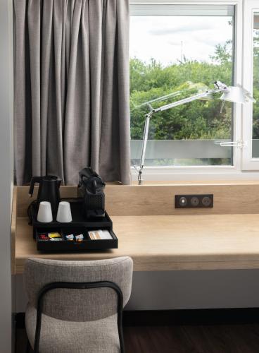 a desk with a coffee maker and a window at Campanile NATURE - Bordeaux Sud Gradignan Talence in Gradignan