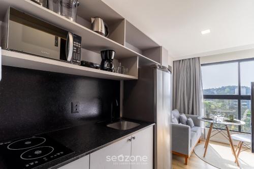 a kitchen with a stove top oven next to a living room at RUP - Studios Equipados em Prédio com Piscina in Blumenau