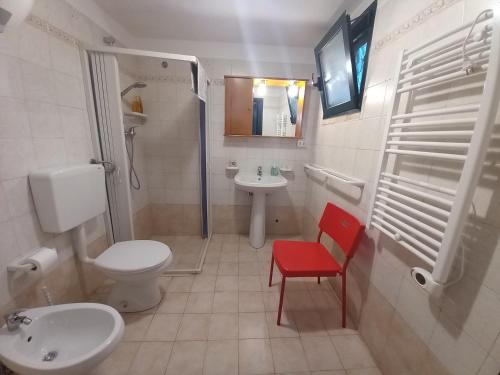 a bathroom with a toilet a sink and a red chair at Breezes B&B in Conca Specchiulla