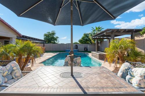 a table with an umbrella in front of a swimming pool at Sunny Home with Backyard Oasis in San Tan Valley! in Queen Creek